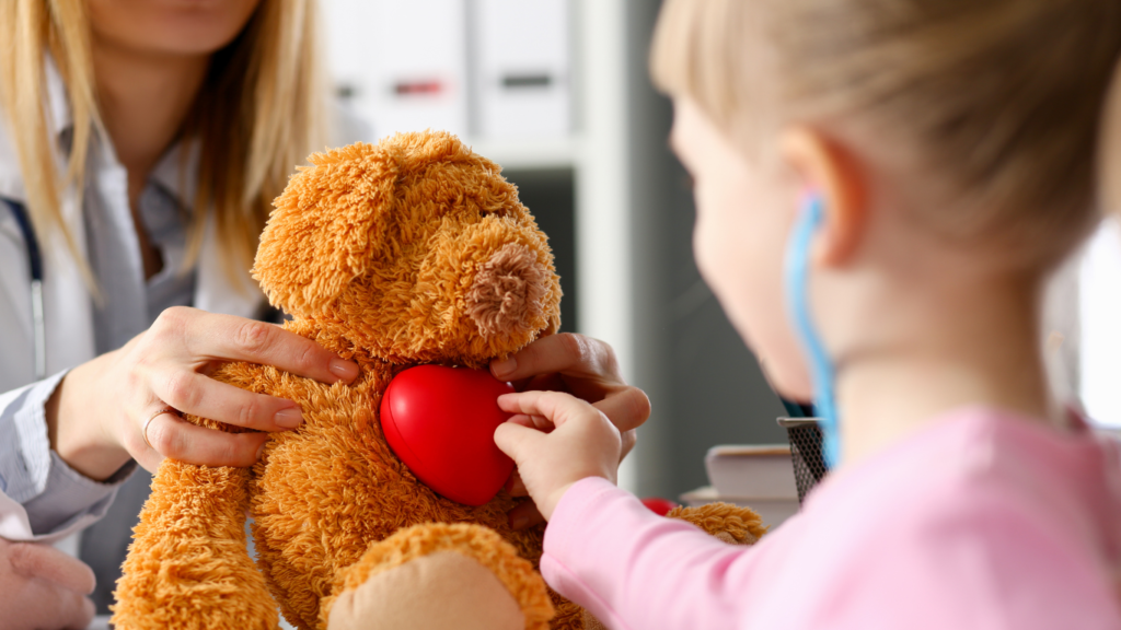 Criança usando estetoscópio para ouvir coração de ursinho de pelúcia em consulta pediátrica